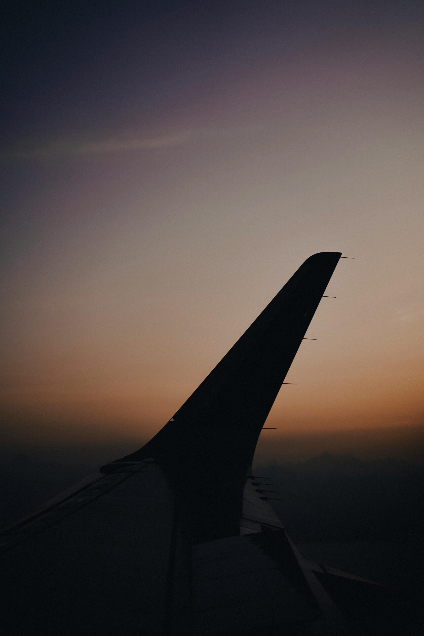 Silhouette of an airplane wing against a colorful sunset sky, highlighting travel themes.